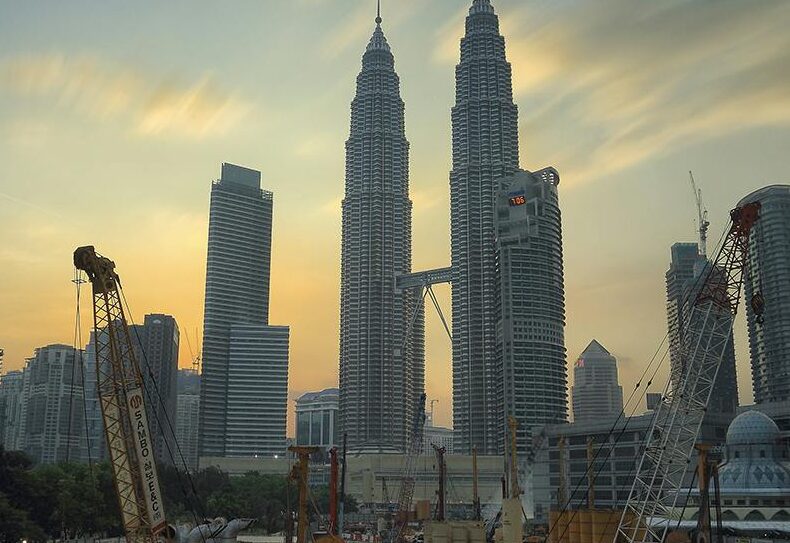 Dramatic view of the Petronas Towers towering over a busy construction site in Kuala Lumpur at sunset.